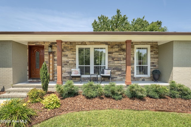 doorway to property with covered porch, brick siding, and stone siding