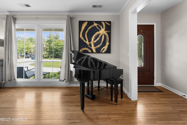 foyer entrance with crown molding, baseboards, wood finished floors, and visible vents