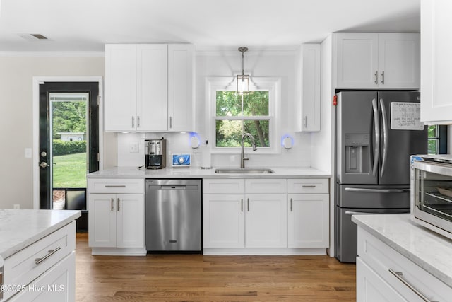 kitchen with ornamental molding, white cabinetry, a sink, appliances with stainless steel finishes, and backsplash