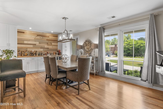 dining area with crown molding, an inviting chandelier, light wood finished floors, wood walls, and recessed lighting