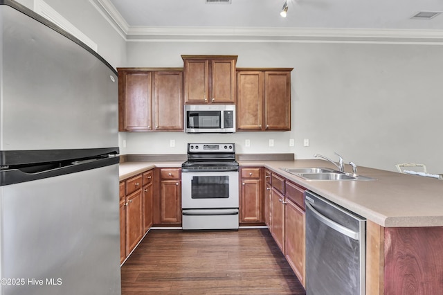 kitchen with crown molding, brown cabinets, appliances with stainless steel finishes, a sink, and a peninsula