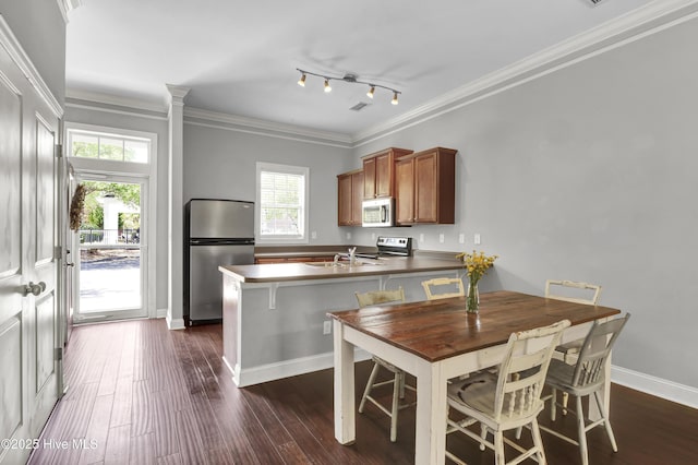 kitchen featuring brown cabinetry, stainless steel appliances, a peninsula, dark wood-type flooring, and ornamental molding