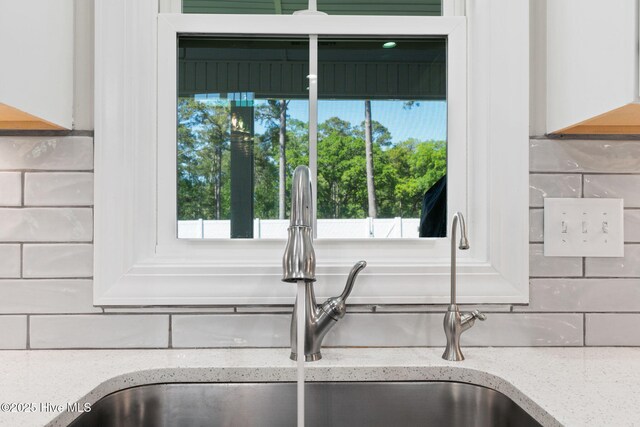 interior details featuring light stone counters, a sink, and backsplash