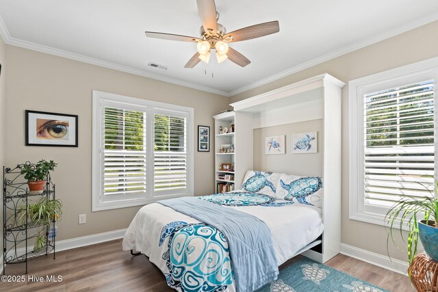 bedroom featuring a ceiling fan, visible vents, wood finished floors, baseboards, and ornamental molding