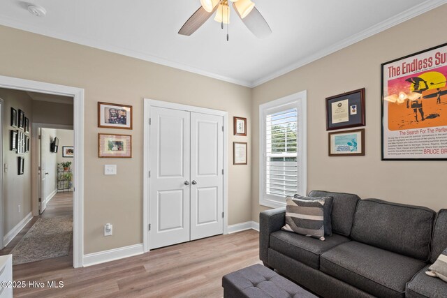 living area featuring light wood-style floors, ornamental molding, baseboards, and ceiling fan