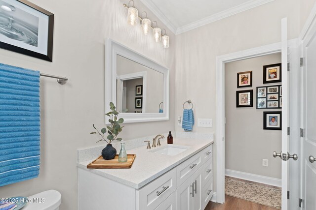 half bathroom with crown molding, toilet, baseboards, and vanity