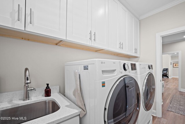 clothes washing area featuring cabinet space, a sink, separate washer and dryer, wood finished floors, and ornamental molding