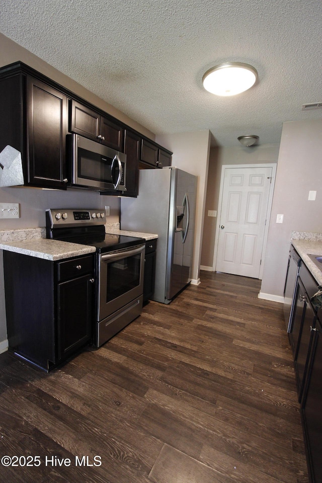 kitchen with stainless steel appliances, dark wood-style flooring, a textured ceiling, and visible vents
