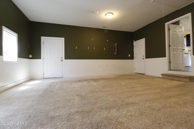 carpeted spare room with attic access and a wainscoted wall
