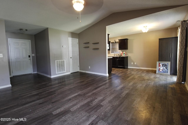 empty room featuring ceiling fan, visible vents, baseboards, dark wood-style floors, and lofted ceiling