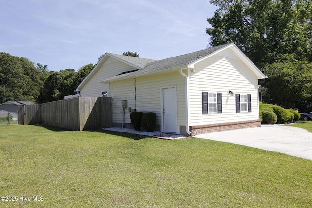 view of side of home with a lawn, a shingled roof, and fence