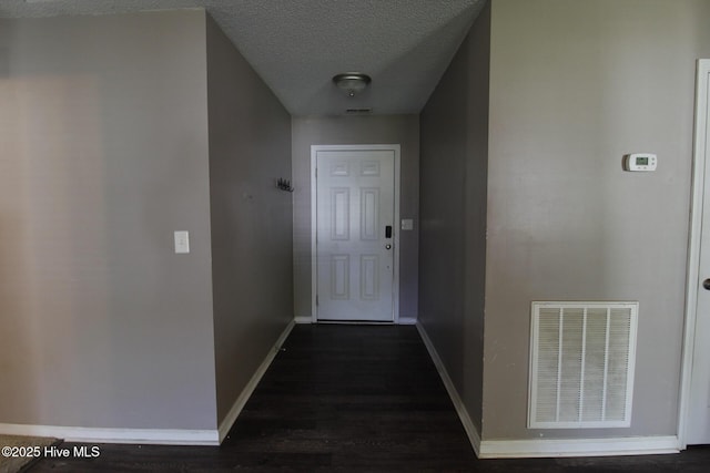 corridor featuring baseboards, dark wood-type flooring, a textured ceiling, and visible vents