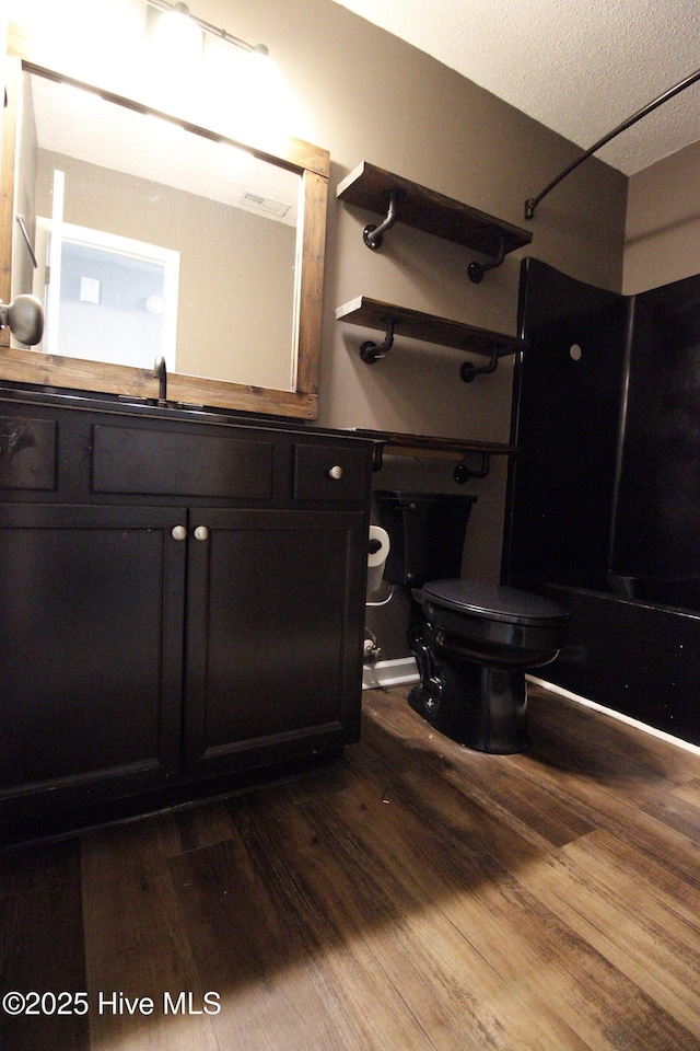 full bathroom with vanity, toilet, a textured ceiling, wood finished floors, and  shower combination