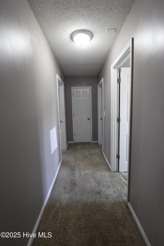 corridor with carpet floors, a textured ceiling, and baseboards