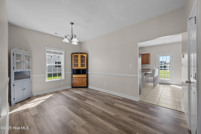 unfurnished dining area featuring an inviting chandelier, baseboards, and wood finished floors