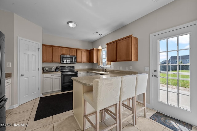 kitchen with black range with electric cooktop, a peninsula, light tile patterned flooring, stainless steel microwave, and a sink