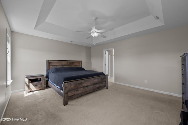 bedroom featuring a ceiling fan, baseboards, light carpet, and a tray ceiling