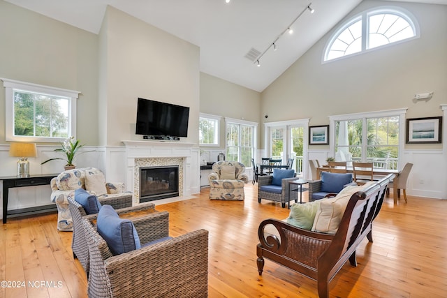 living room featuring track lighting, visible vents, high vaulted ceiling, a fireplace with flush hearth, and light wood finished floors