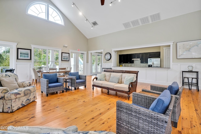 living area with light wood-style floors, a decorative wall, rail lighting, high vaulted ceiling, and visible vents