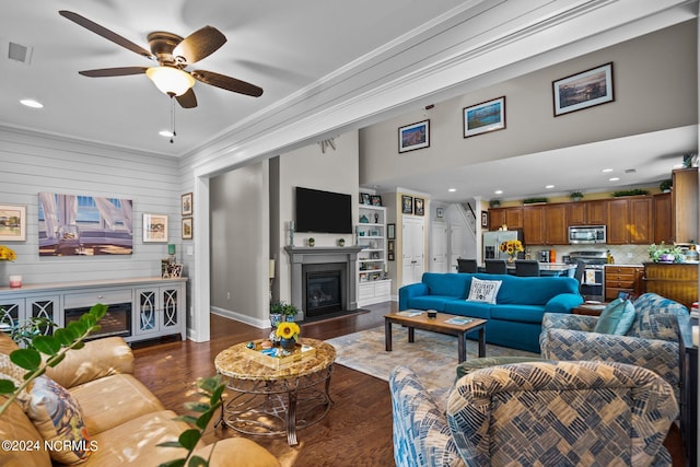 living room featuring ceiling fan, a glass covered fireplace, wood finished floors, visible vents, and ornamental molding