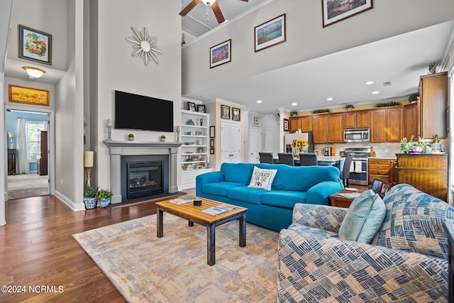 living area featuring a ceiling fan, a towering ceiling, crown molding, dark wood finished floors, and a glass covered fireplace