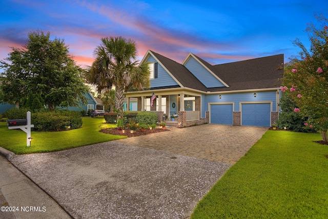 view of front facade with covered porch, decorative driveway, brick siding, a front lawn, and an attached garage
