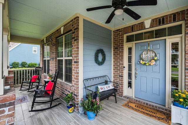 view of exterior entry featuring brick siding, ceiling fan, and covered porch