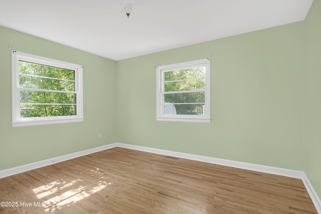 spare room featuring baseboards, wood finished floors, a wealth of natural light, and visible vents