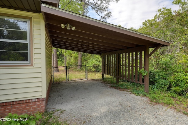 view of vehicle parking featuring driveway, fence, a gate, and a carport