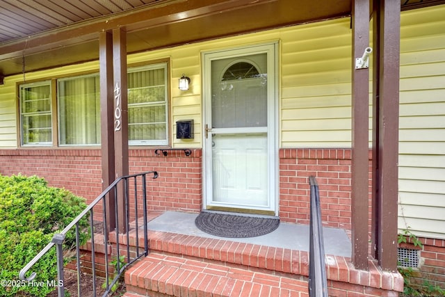 doorway to property featuring covered porch and brick siding