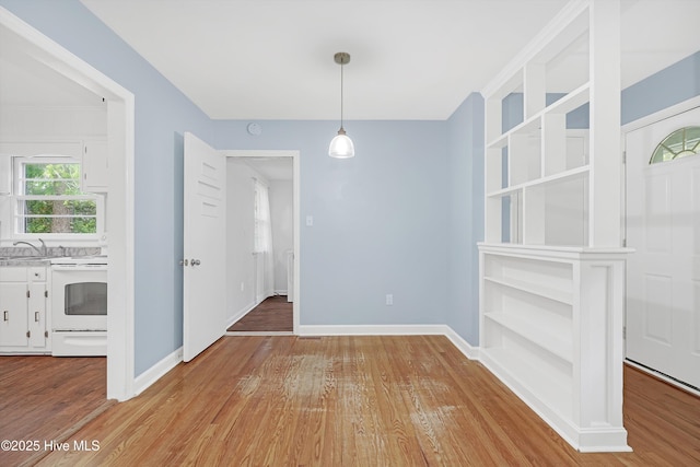 unfurnished dining area with baseboards, a sink, and wood finished floors
