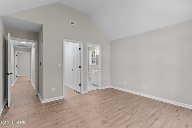 unfurnished bedroom featuring ensuite bath, light wood-style floors, baseboards, vaulted ceiling, and visible vents