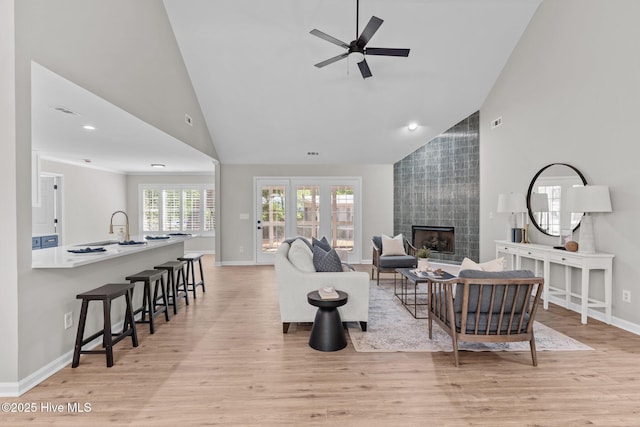 living area featuring light wood-type flooring, baseboards, high vaulted ceiling, and a tile fireplace