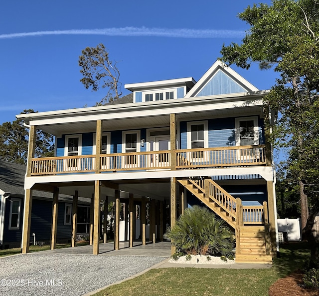 rear view of property featuring a porch, board and batten siding, a carport, gravel driveway, and stairs