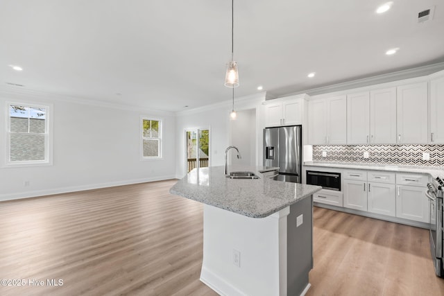 226 NE 64th St, Oak Island, NC 28465 - kitchen featuring appliances with stainless steel finishes, a sink, ornamental molding, a kitchen island with sink, and white cabinets
