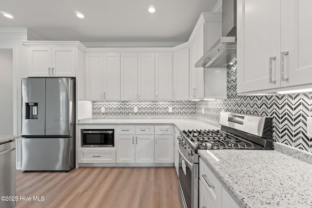 226 NE 64th St, Oak Island, NC 28465 - kitchen with appliances with stainless steel finishes, wall chimney range hood, white cabinetry, light wood finished floors, and recessed lighting