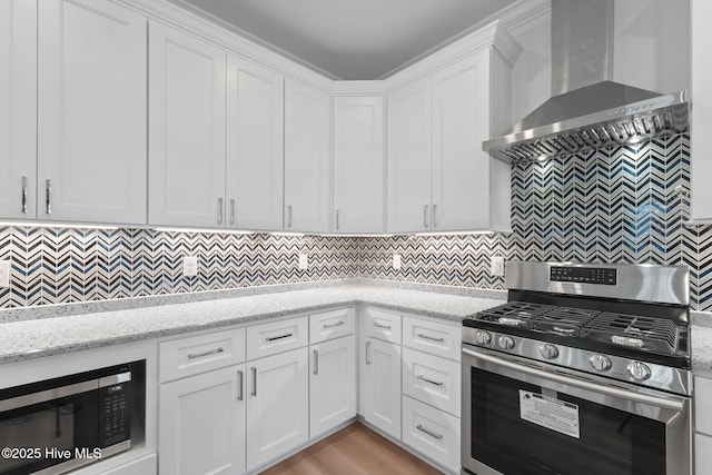 226 NE 64th St, Oak Island, NC 28465 - kitchen featuring stainless steel appliances, wall chimney range hood, white cabinetry, backsplash, and light stone countertops