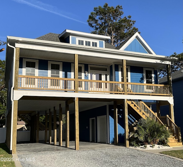 coastal home featuring stairs, covered porch, board and batten siding, a carport, and gravel driveway