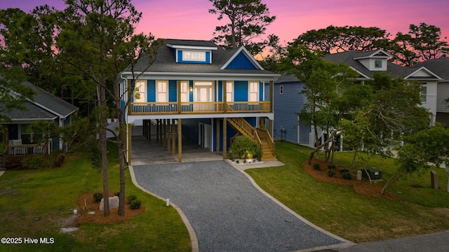 226 NE 64th St, Oak Island, NC 28465 - coastal inspired home featuring a carport, gravel driveway, a lawn, stairway, and a porch