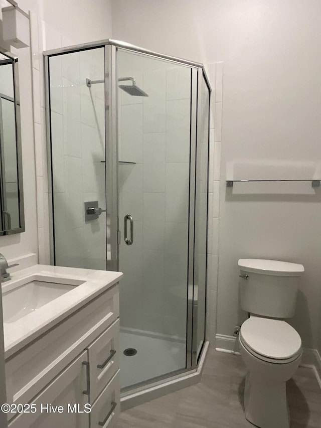 full bath featuring vanity, baseboards, a shower stall, and toilet