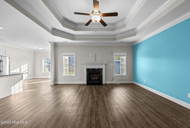 unfurnished living room with ornamental molding, wood finished floors, ceiling fan, a raised ceiling, and a fireplace with flush hearth