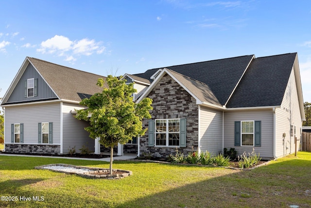 view of front of home featuring a shingled roof, a front yard, and stone siding