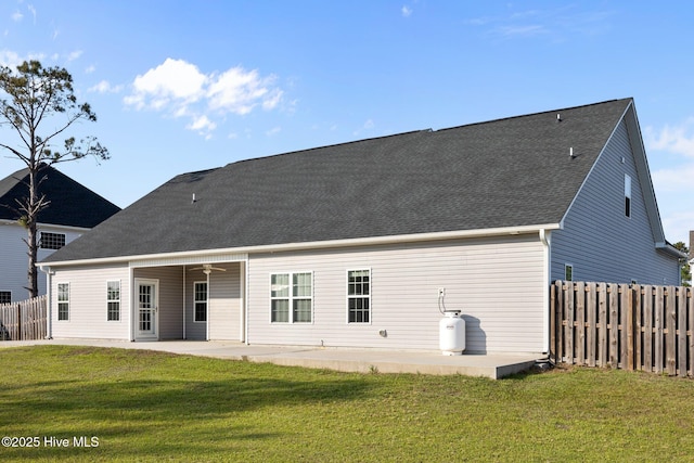 back of property with a ceiling fan, a patio area, fence, a yard, and a shingled roof