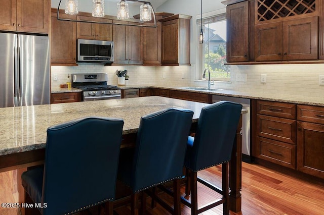 kitchen featuring decorative backsplash, a kitchen breakfast bar, a sink, light wood-style floors, and stainless steel appliances