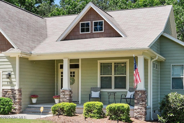 entrance to property with roof with shingles, covered porch, and stone siding