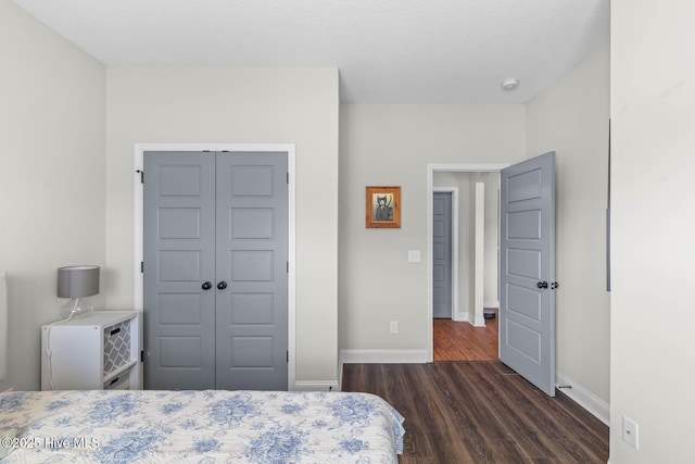 bedroom featuring dark wood-style flooring, baseboards, and a closet