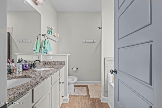 bathroom featuring a sink, toilet, double vanity, baseboards, and wood finished floors