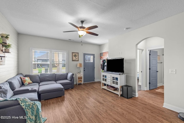 living room featuring arched walkways, a textured ceiling, a ceiling fan, and wood finished floors
