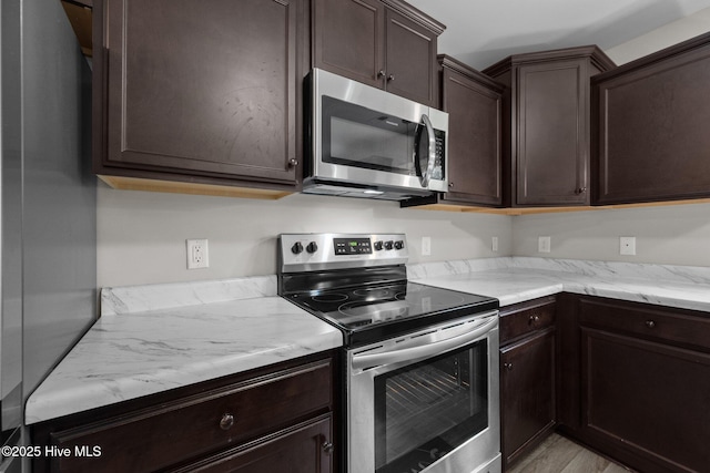 kitchen with light wood-style floors, light stone countertops, stainless steel appliances, and dark brown cabinets