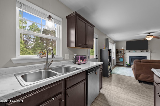 kitchen featuring dark brown cabinetry, stainless steel dishwasher, a fireplace, light countertops, and a sink